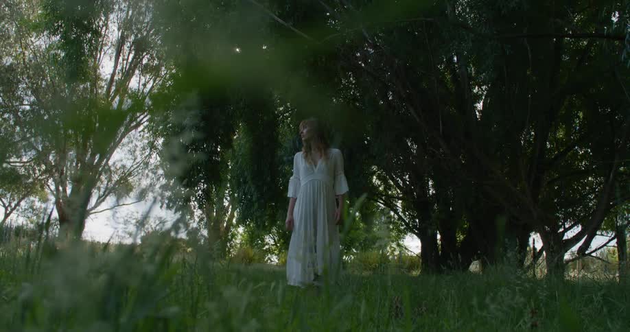 Woman in white dress walks through trees in field
