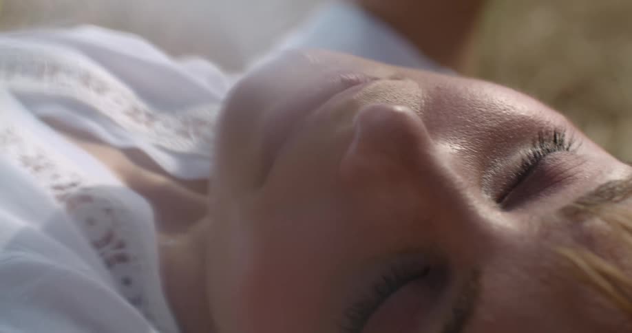 A woman lying in grass turns her head as the sun shines down on her