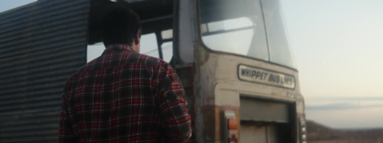 A man walks toward an abandoned bus in a field