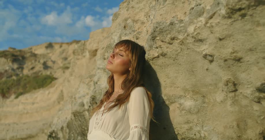 A woman leans against a canyon wall with her eyes closed