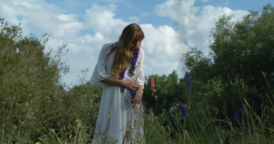 A woman in a white dress poses behind wildflowers in the woods