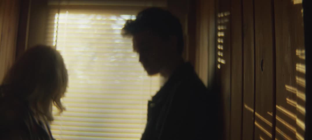 Man and woman stand in corridor silhouetted against sunlight coming through blinds