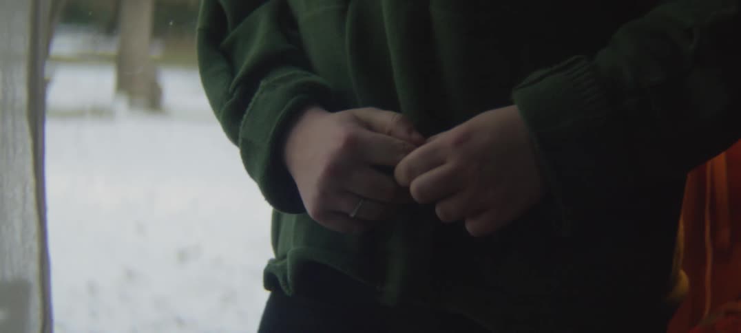 A person wearing a coat is standing outside holding their hands and fingers