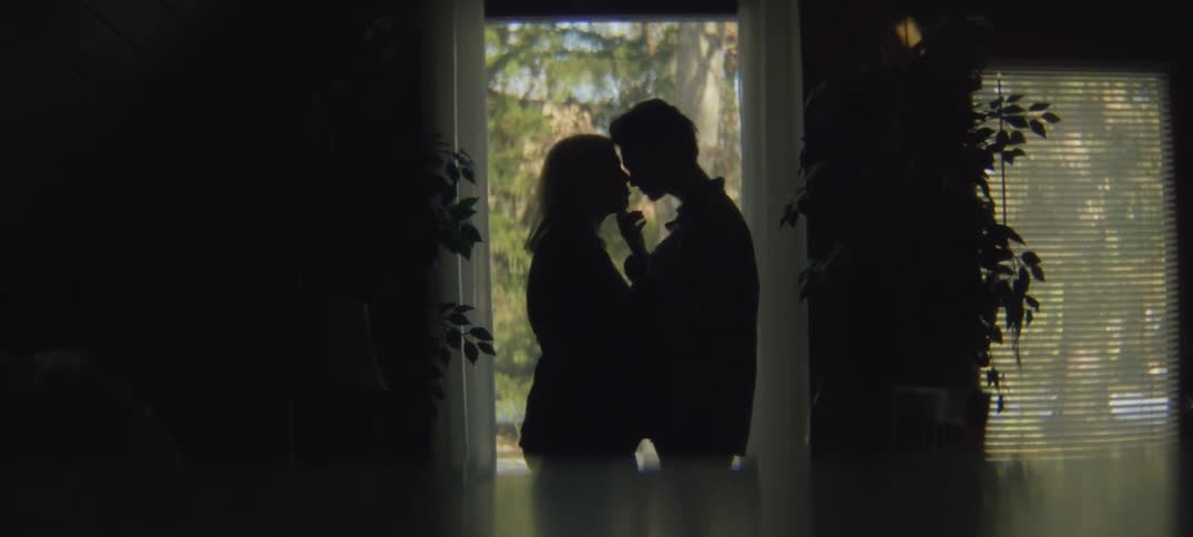A man and woman stand in a doorway of a home and hug and put their foreheads together