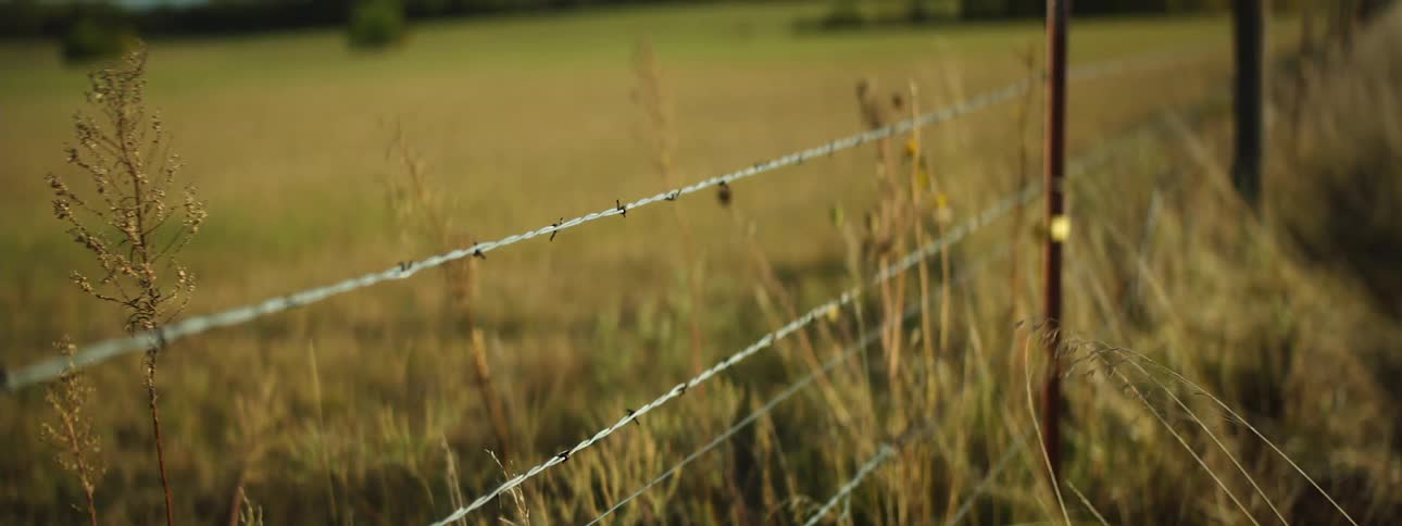 A barbed wire fence in a large field during the day