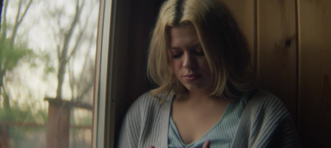 A woman stands next to a window holding a mug