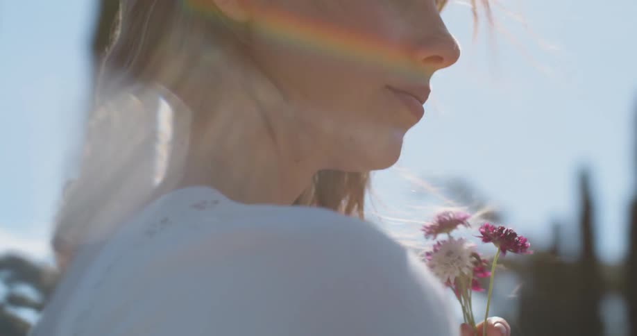 A woman carrying flowers walks outdoors as the wind blows her hair