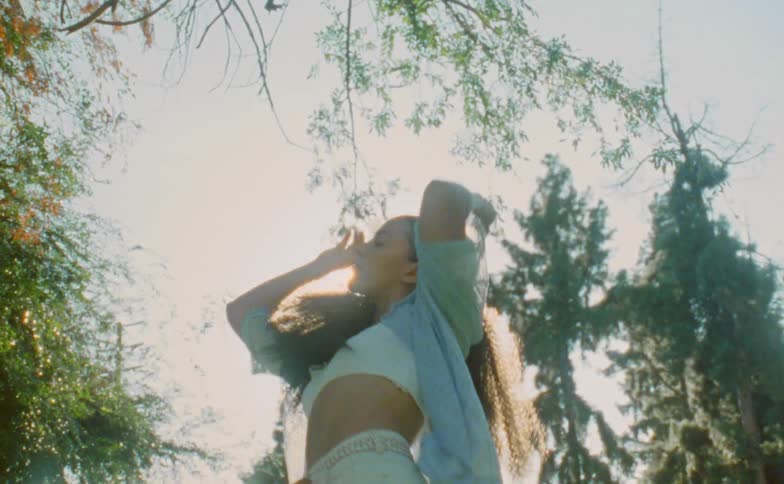 The sun shines upon a teenage girl standing outside dancing and spinning around near trees