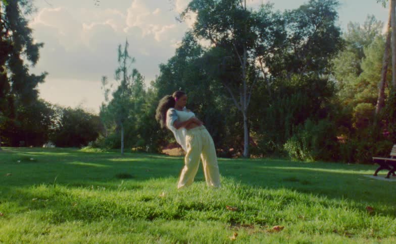 Female dancer with ponytail blue shirt white top and beige pants dances in public park