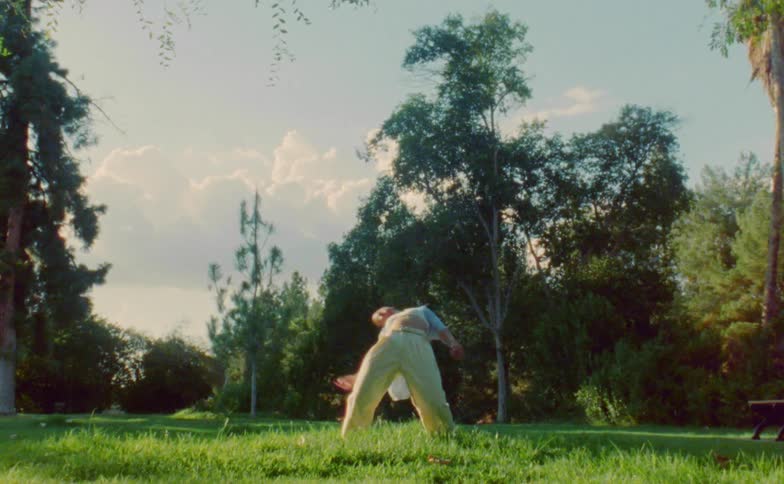 The sun shines upon a teenage girl standing outside dancing near trees and woods in a park