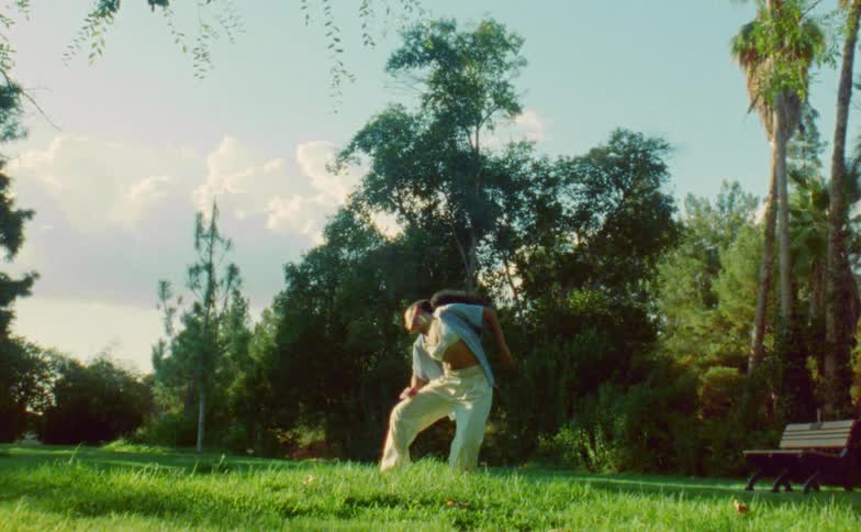 The sun shines upon a teenage girl standing outside dancing near trees and woods in a park