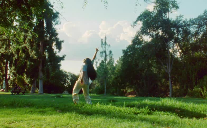 Female dancer with ponytail blue shirt white top and beige pants dances in public park