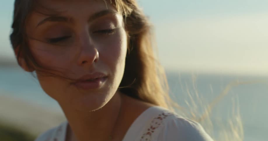 A teenage girl is walking along the coast and turns to look behind her as her hair blows in the wind
