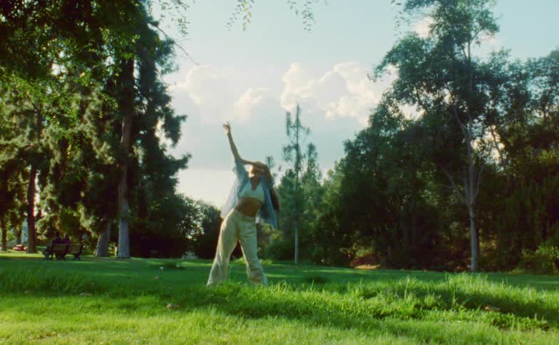 The sun shines upon a woman standing outside dancing near trees in the woods