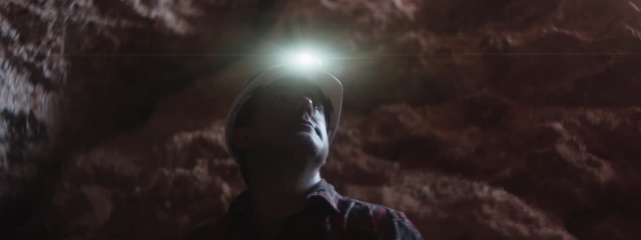 A man wearing a helmet with a headlamp looks up at the surrounding rock walls