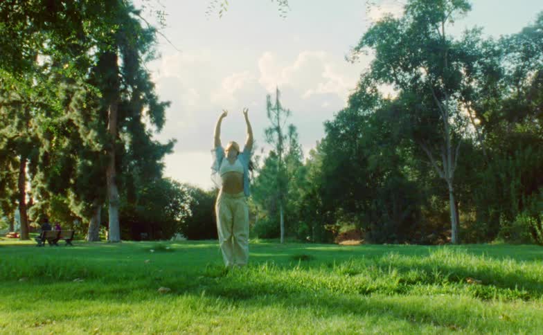 A woman raises her arms while performing a modern dance in a park