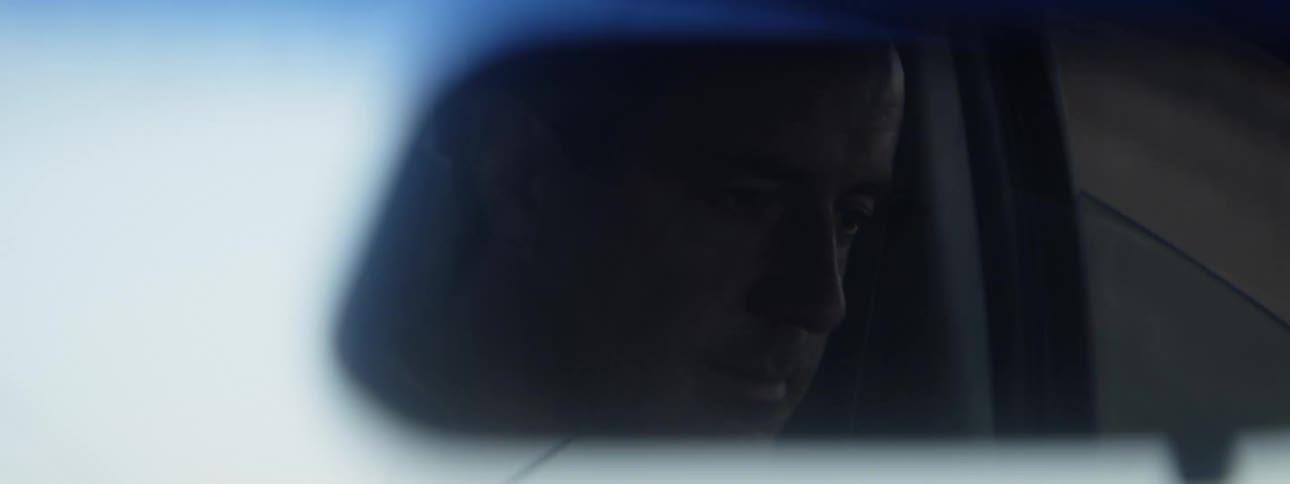 A mans face in a rearview mirror as he drives