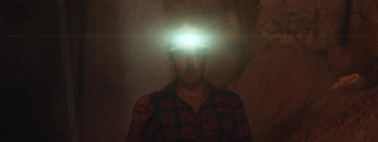 Miner with miner hard hat with light carries pickax over shoulder in mine