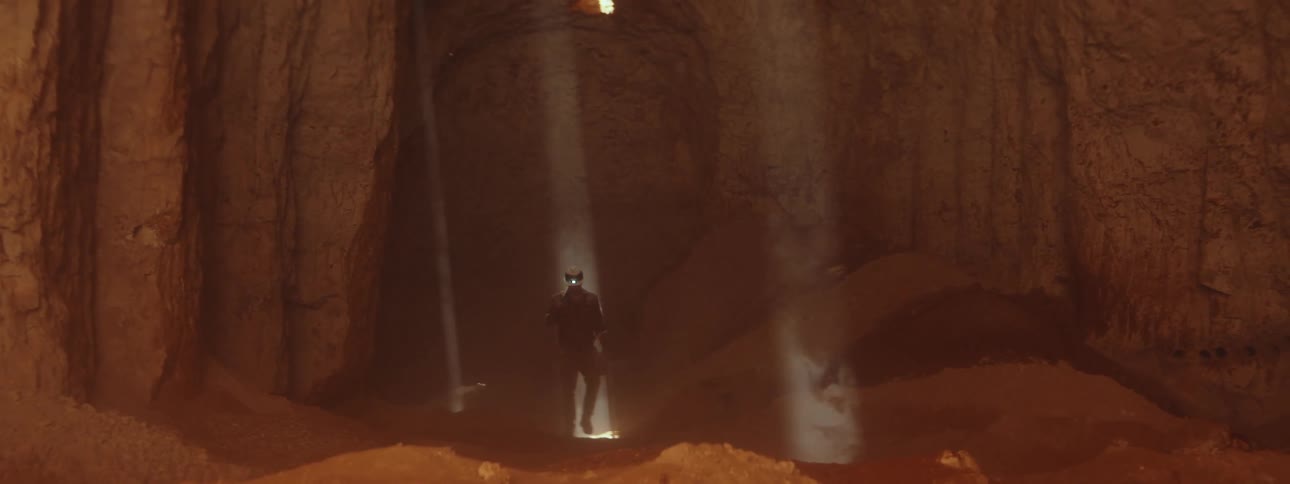 Person wearing headlamp walks through sun rays entering cavern