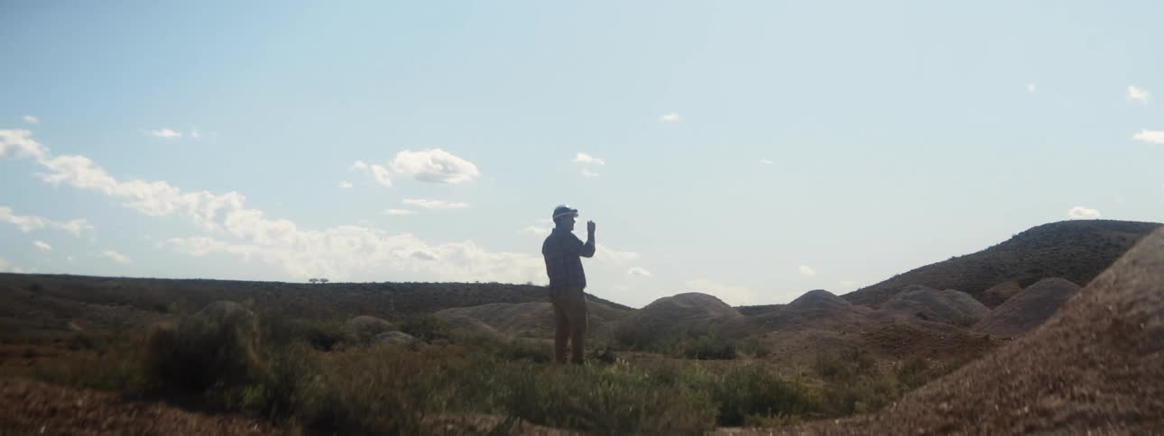 Man wearing headlamp stands in hilly terrain under a cloudy sky