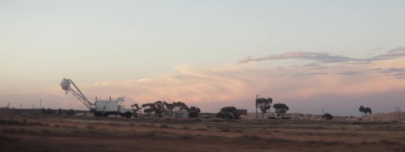 Vehicle drives across the field with a few trees and a blower at dusk