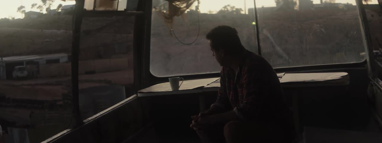 A man sits at a table with a mug and looks out the window