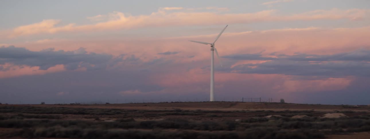 Wind turbine stands in field against red tinted clouds