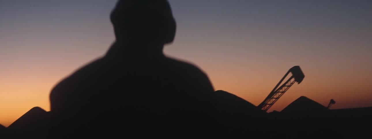 Silhouette of a man walking toward digging equipment and piles of soil