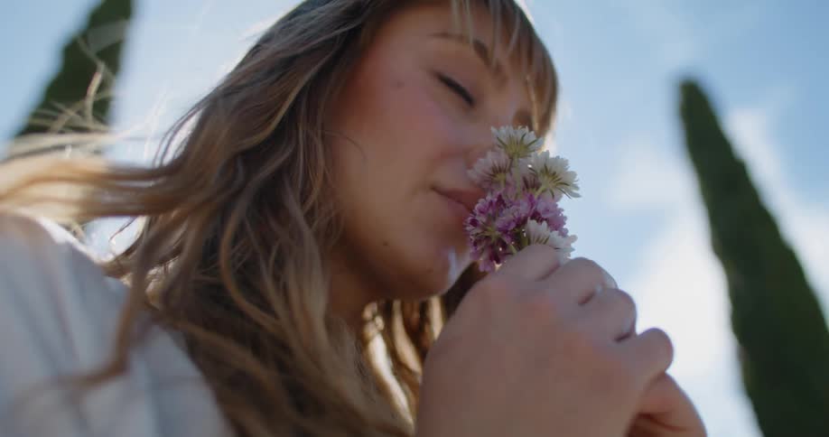 A woman sniffs a handful of flowers while standing outdoors on a windy day