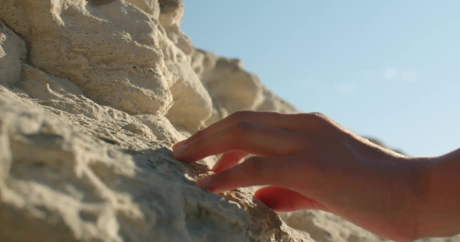 Fingers touch white rock cliff wall in awe on a bright sunny day