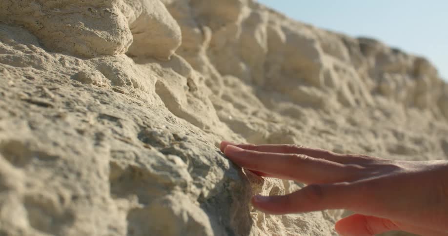 A woman runs her hand across a large rock