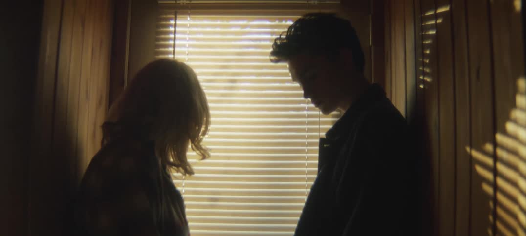 Light shining through blinds casts shadows of man and woman standing in the hallway
