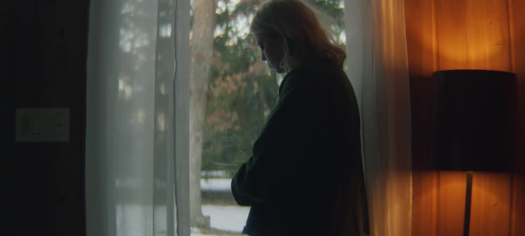 Woman stands near window showing view of snow covered yard