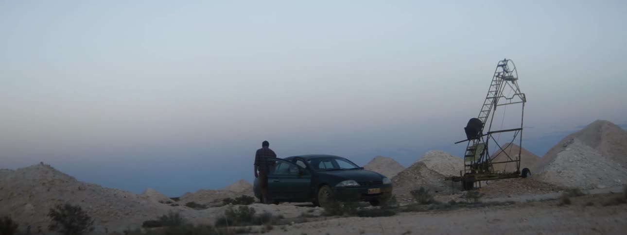 Man exits car near metal structure sitting among dirt mounds