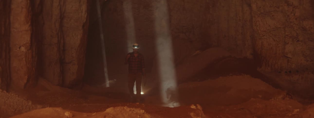 A man is walking in an underground mine with a headlamp on his hardhat