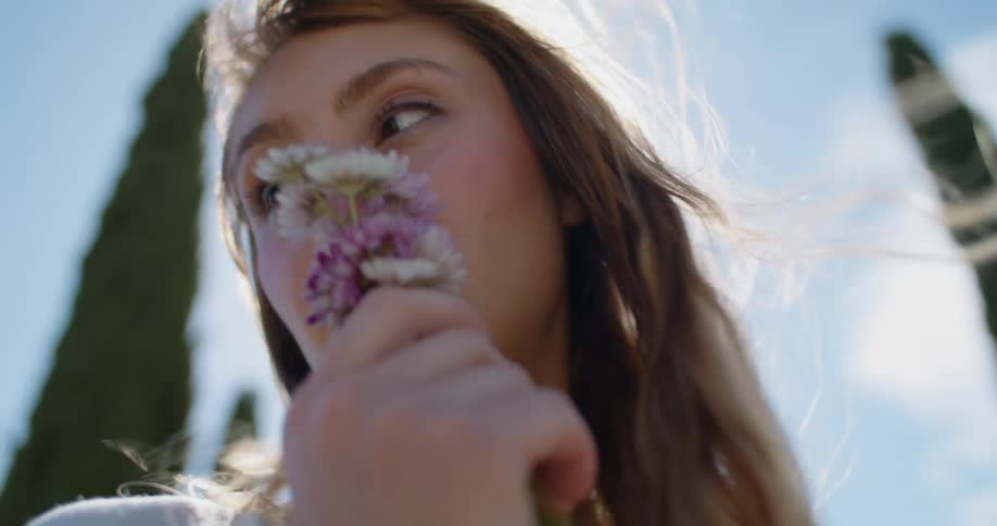 A woman smells flowers outside as the wind blows her hair