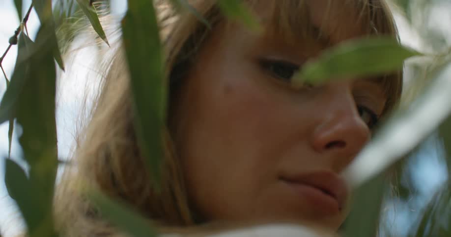 A woman stands amidst the leaves of a tree while looking directly into the camera