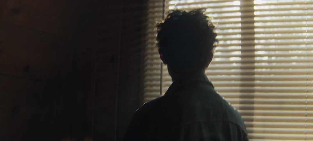 A young man paces and runs his hands through his hair before looking through the blinds
