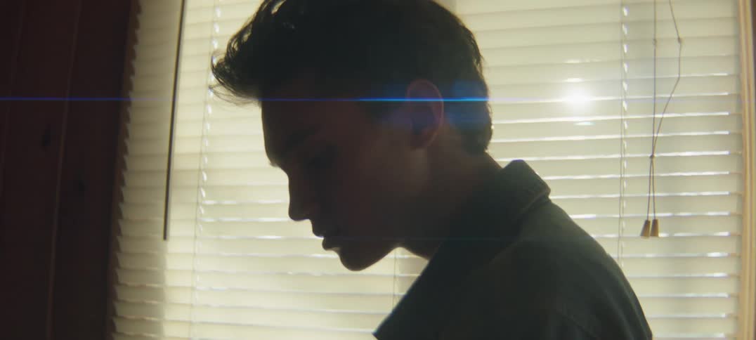 Side profile of man wearing shirt standing next to windowblinds at sunset