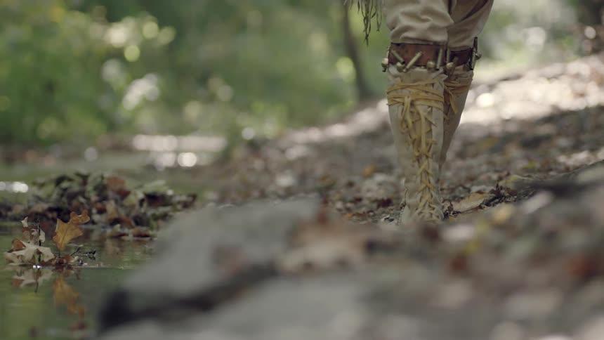 A person in long boots walks near a creek bed in the day time