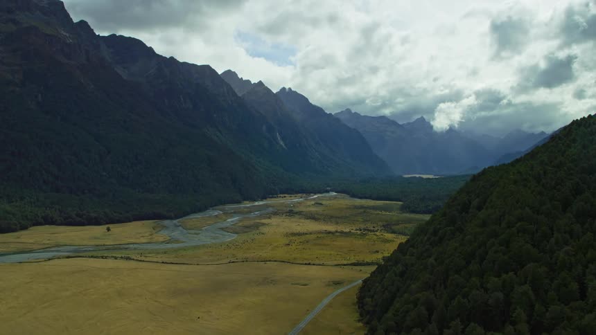 Road and river cut through valley between tall mountains on cloudy day