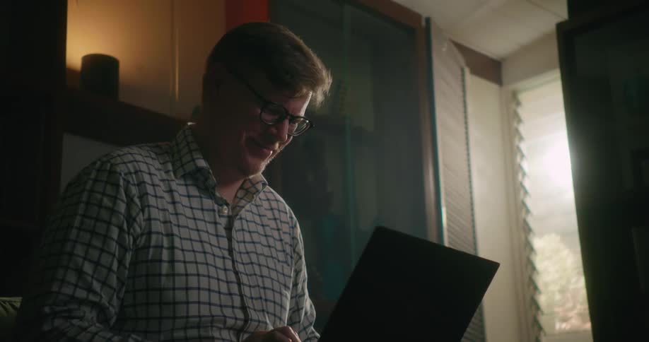 Man sits at home in living room using laptop and smiling