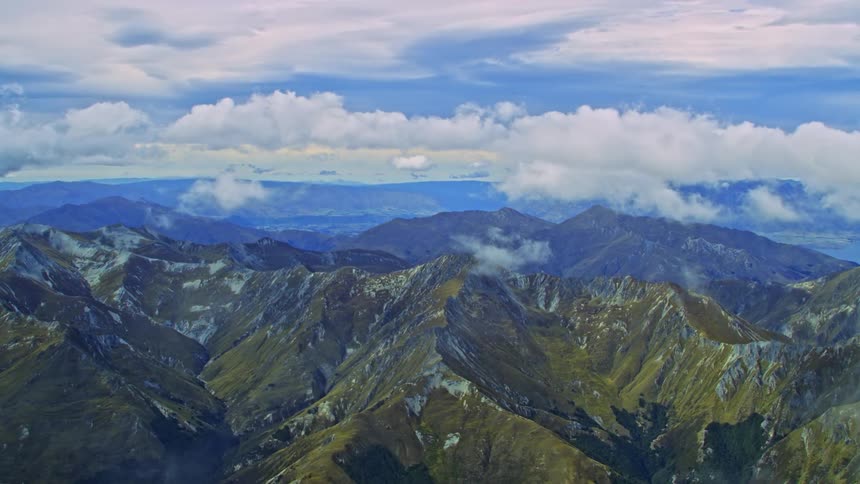 Flying through light clouds towards rugged mountain peaks