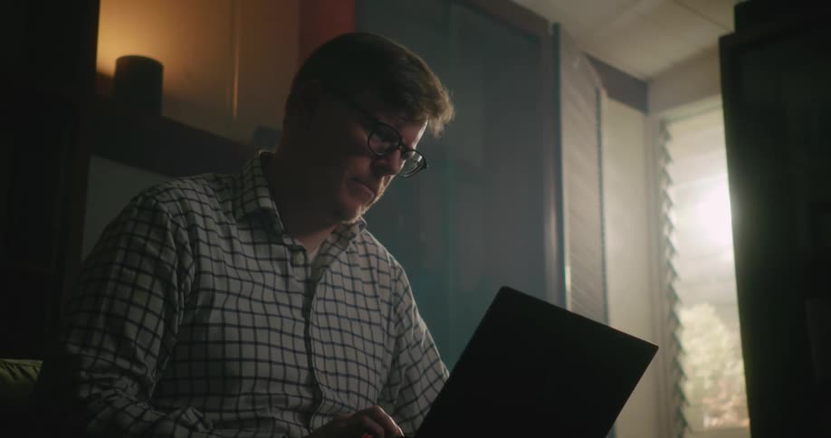 A man nods his head as he thinks then begins to type on a laptop sitting near a window