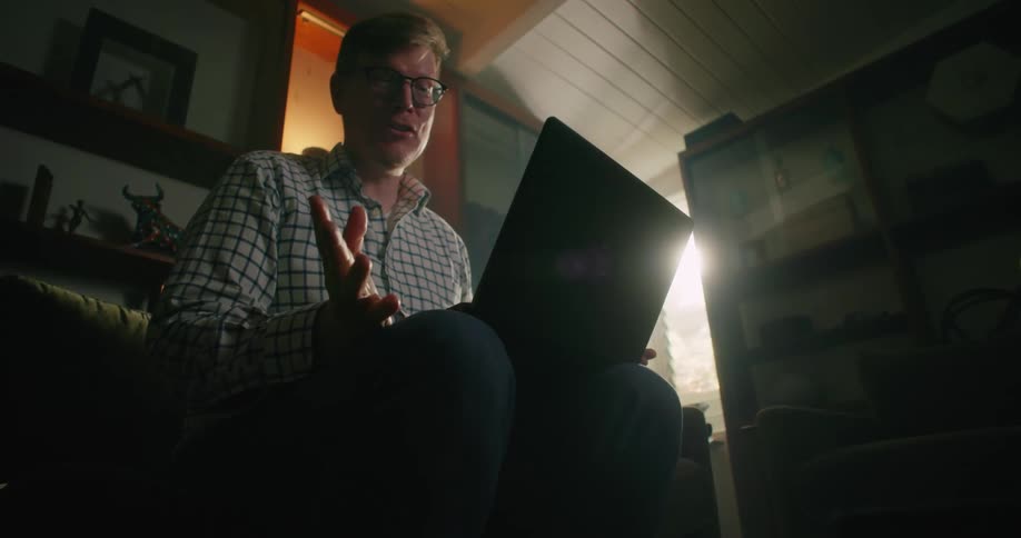A man sits at home with a laptop on his knee and video chats