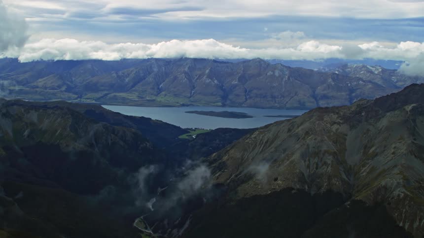 An aerial view flying through clouds over a mountain range towards a lake
