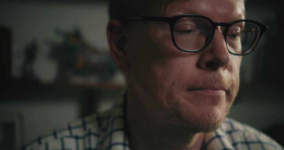 A man wearing glasses looks up and makes a face as he is thinking then appears to have an idea and looks down again