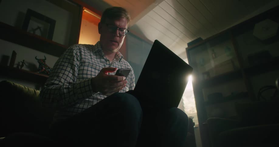 Man frowns at smartphone puts it down and continues working on laptop