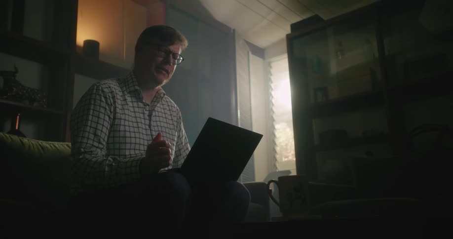 A man holding a laptop on his lap is talking to someone