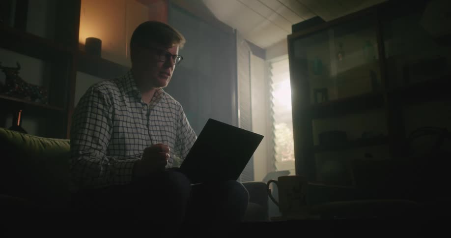A man is sitting on the couch with his laptop computer talking as he has a video conference